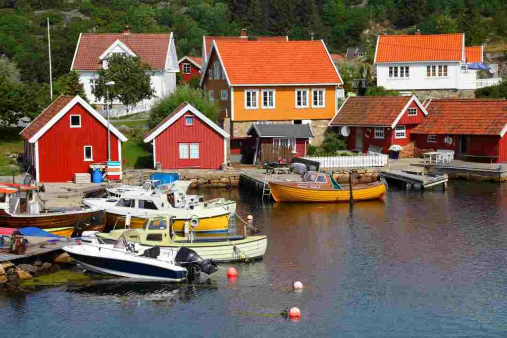 Typical coastal village around Kristiansand in the south of Norway, with colorful wooden houses and docks and small boats. 