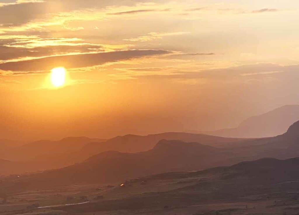 A golden sunset over a mountain plain in central norway, the hills rolling into infinity colored golden maroon, and the sun is a fireball in the sky, coloring the sky and clouds in golden shades