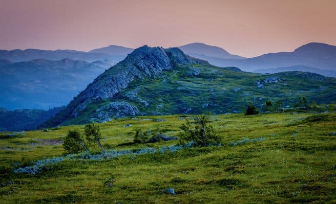 The green mountain plains of Gaustablikk in Norway, against a backdrop of hilly mountains in the distance with a pink sky behind it as the sun has just set