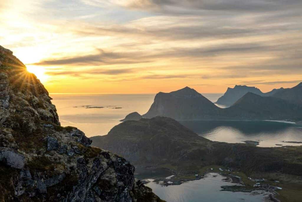 The golden midnight sun shining on the mountains of Lofoten against a backdrop of a calm shiny sea. 