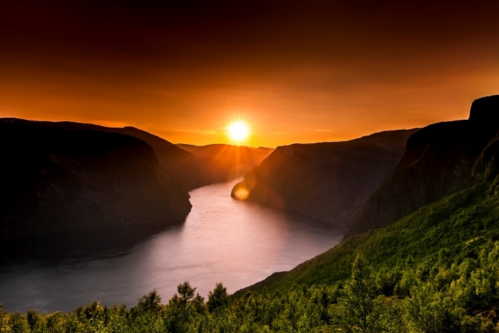 The midnight sun over a silvery blank fjord in Norway with steep mountains on all sides