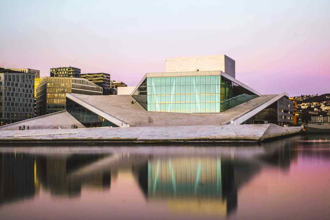 Is Oslo worth visiting? The Opera house on a calm day with blank seas in front of the glass facade and glacier style structure under a pale bluish pink sky
