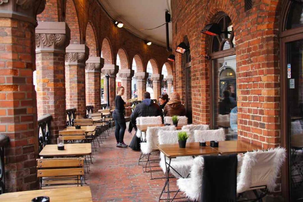 a cozy cafe district surrounded by old red brick architecture, outdoors seating and people enjoying and socializing in Oslo Norway.
