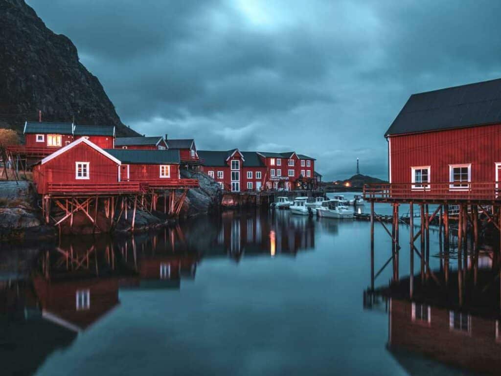 Å in Lofoten ambiance on a day with heavy clouds, still water, and warm lights among the red traditional fishermens cottages above the water. 