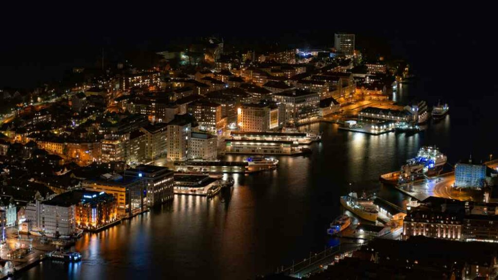 Overview photo of Bergen Norway by night, with the city lit by thousands of lights around the narrow harbor