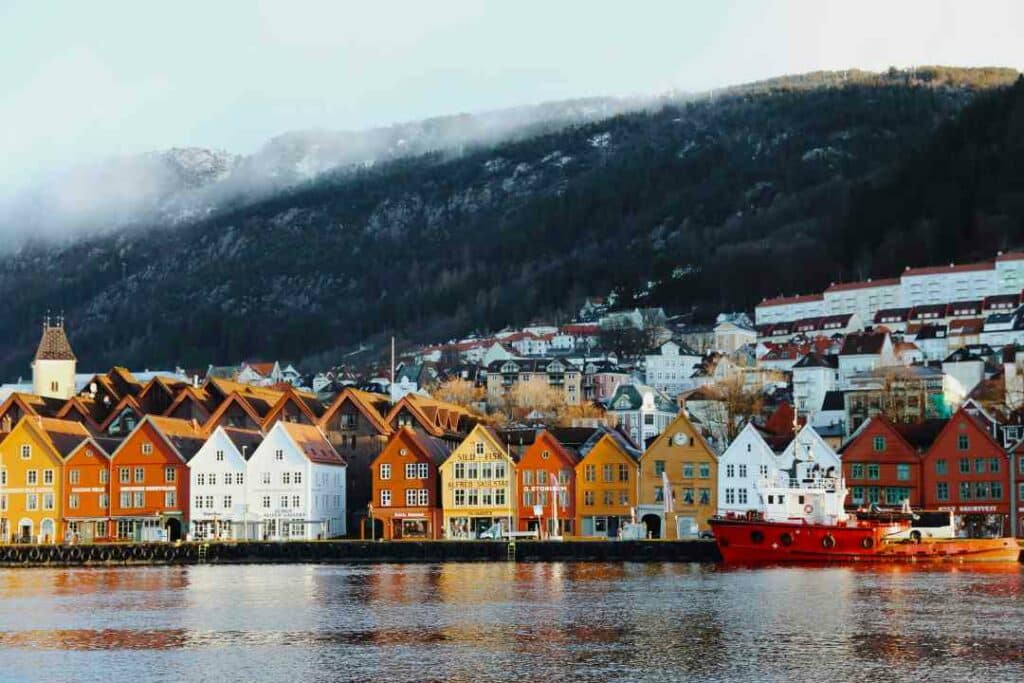 Bryggen i Bergen, the Bergen Jetty with the colorful wooden houses characteristic for Bergen, Norway. The sun is shining on the row of wooden houses, while there are some clouds over the tree covered hills in the background, on a winter day. 