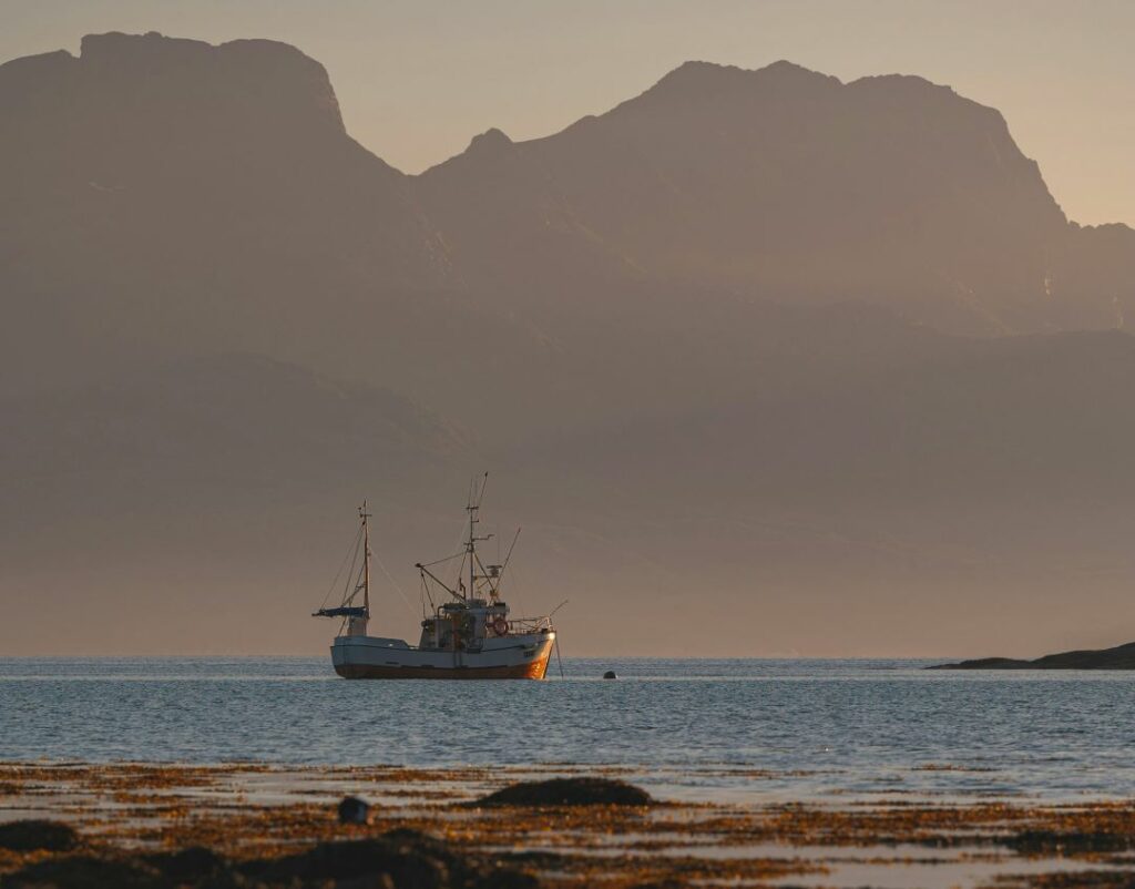 Fishing boat in the warm sun on a blank sea outside Bodo, Norway, with the vast moutnains in the background like a shadow. 