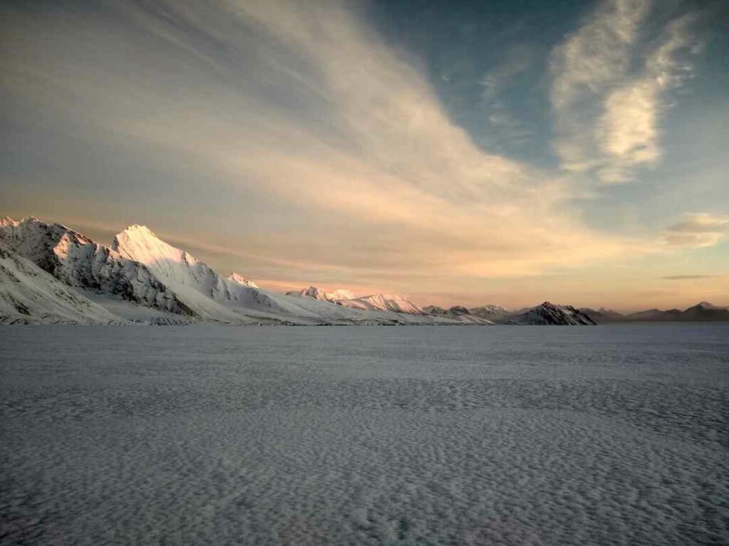 Hansbreen Glacier in Svalbard on a late winter day with a low sun over the snowy mountains and plains under a pale blue sky with floating transparent clouds