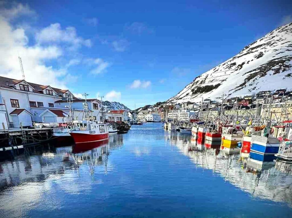 The harbor in Honningsvåg, with a myriad of fishing vessels amidst the houses in the hilly town, below the mountains that are still covered in snow on a cold clear sunny day in early spring