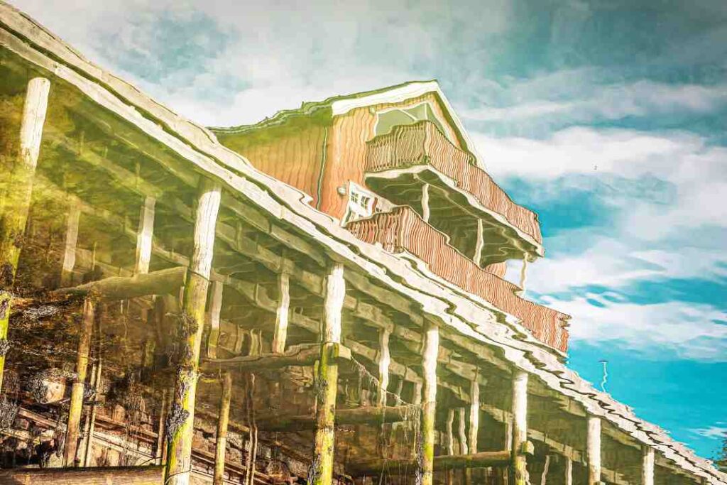 A red wooden cabin on a wooden pier seen through reflections in the water, so in a waivy unclear expression