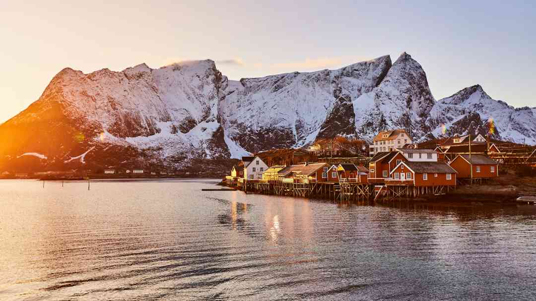 Lofoten with a low winter sun in Norway, glowing on the snow covered mountains and the traditional fishing village with red wooden houses
