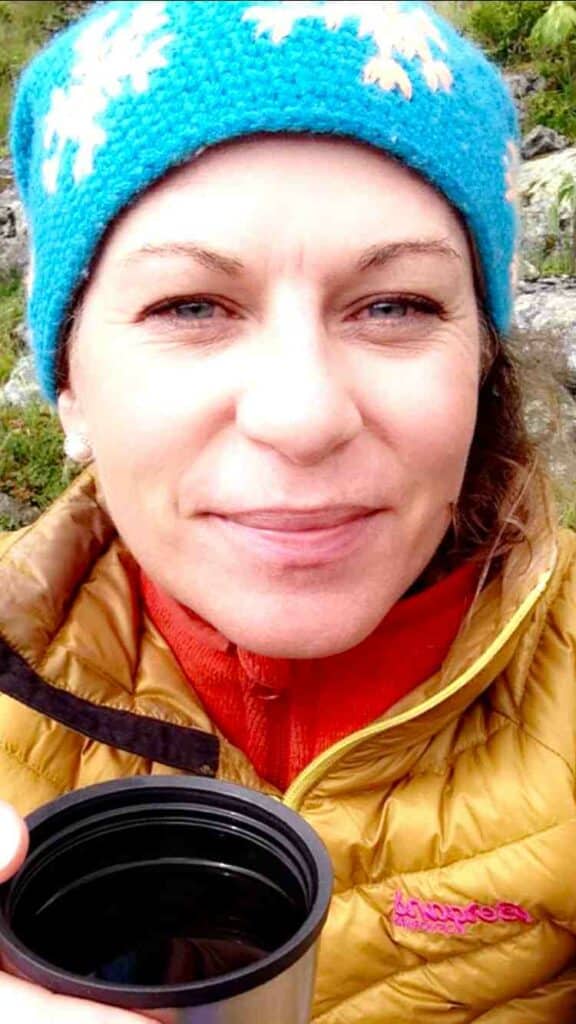 Portrait of Hege Jacobsen with a blue hat, yellow warm winter jacket, and a cup of coffee from a thermos in the mountain during a hike