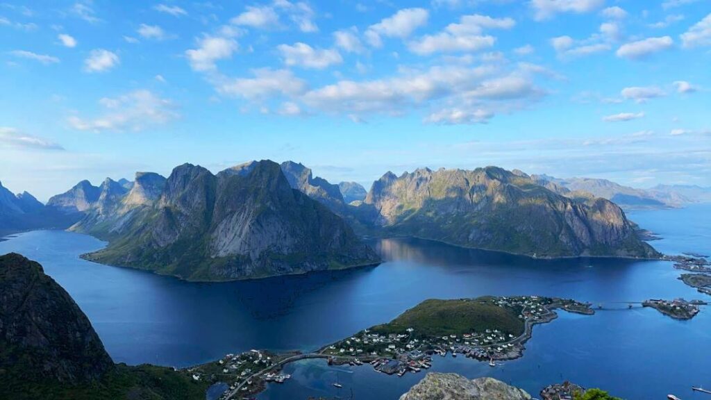 Stunning views of mountains and fjord from the topp of Reinebringen mountain sherpa staris on a sunny day with a pale blue sky, and deep blue waters surrounding the green mountainious islands in Lofoten, Norway. 