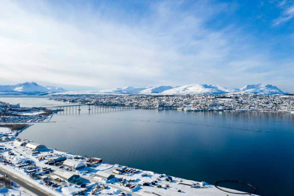 The Tromsø island on a bright day late in winter, with blue sky and sun over the winter city and the white snow capped mountains in the background