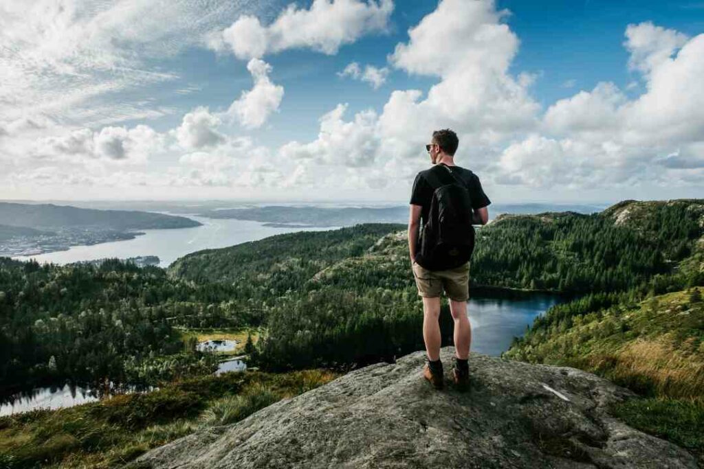 Hiking the Vidden over Bergen Norway, man standing enjoying the view from the green wide hilly Vidden, looking down at the blank fjord and the city far below