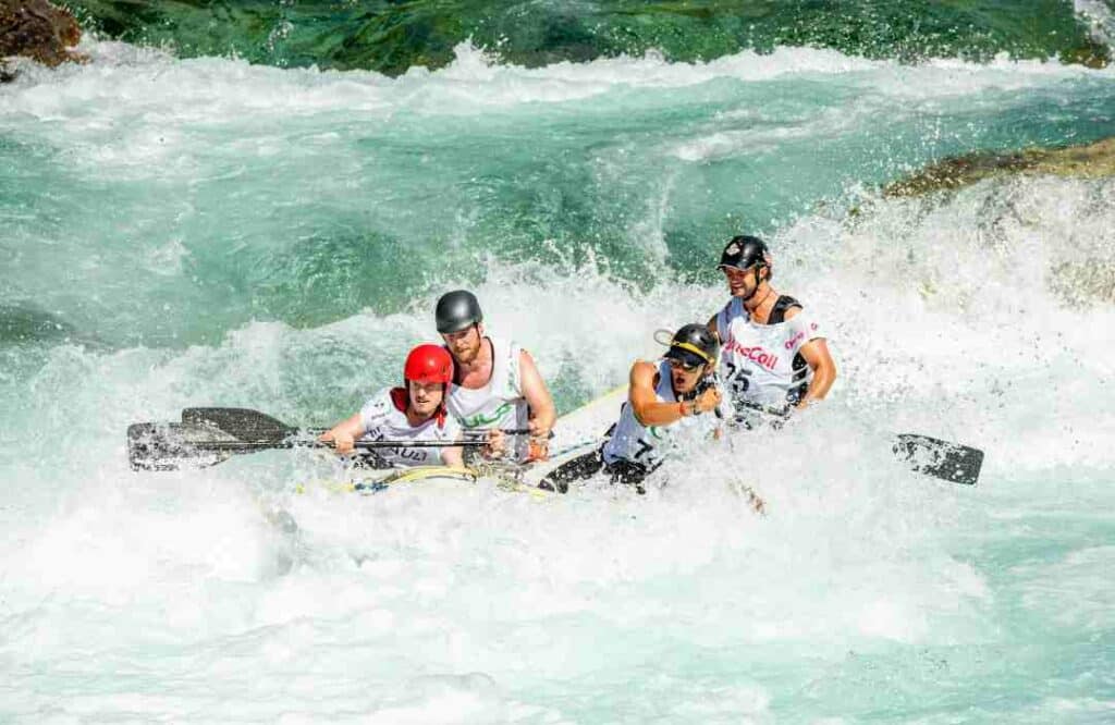 White water rafting in Voss, Norway, a small raft with four people navigating fierce whitewater river passes wearing helmets and paddling on a sunny summer day