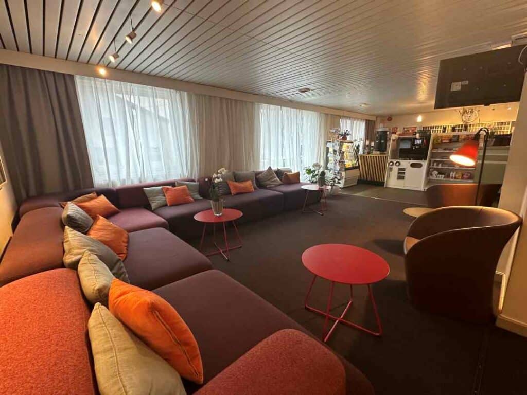 The inviting foyer at Scandic Hotel Honningsvåg with a big soft colorful sofa with pillows, small cute chairs, warm lighting, and a small kiosk in the reception