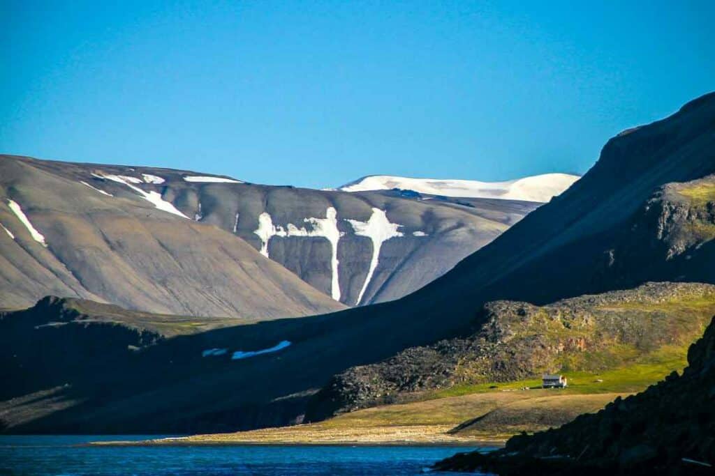 summer scenery in Svalbard, with green plains betwee the dark greyish unique mountains where there are still patches of snow under a deep blue sky - Norway in August