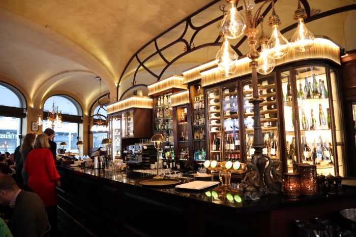 The elegant bar at the Continental hotel in Oslo, with warm lighting and glass shelfs, people enjoying the ambiance