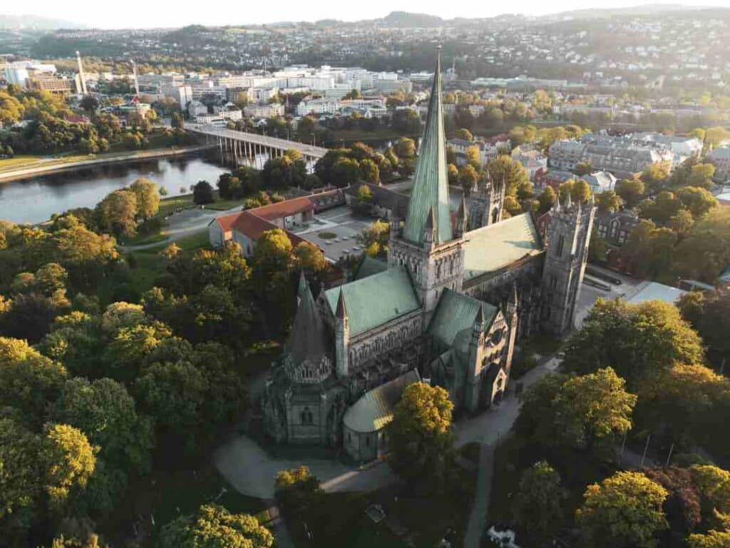 Aerial photo of a dramatic stone cathedral with towers and spears, surrounded by big green trees and parks in the middle of a small town