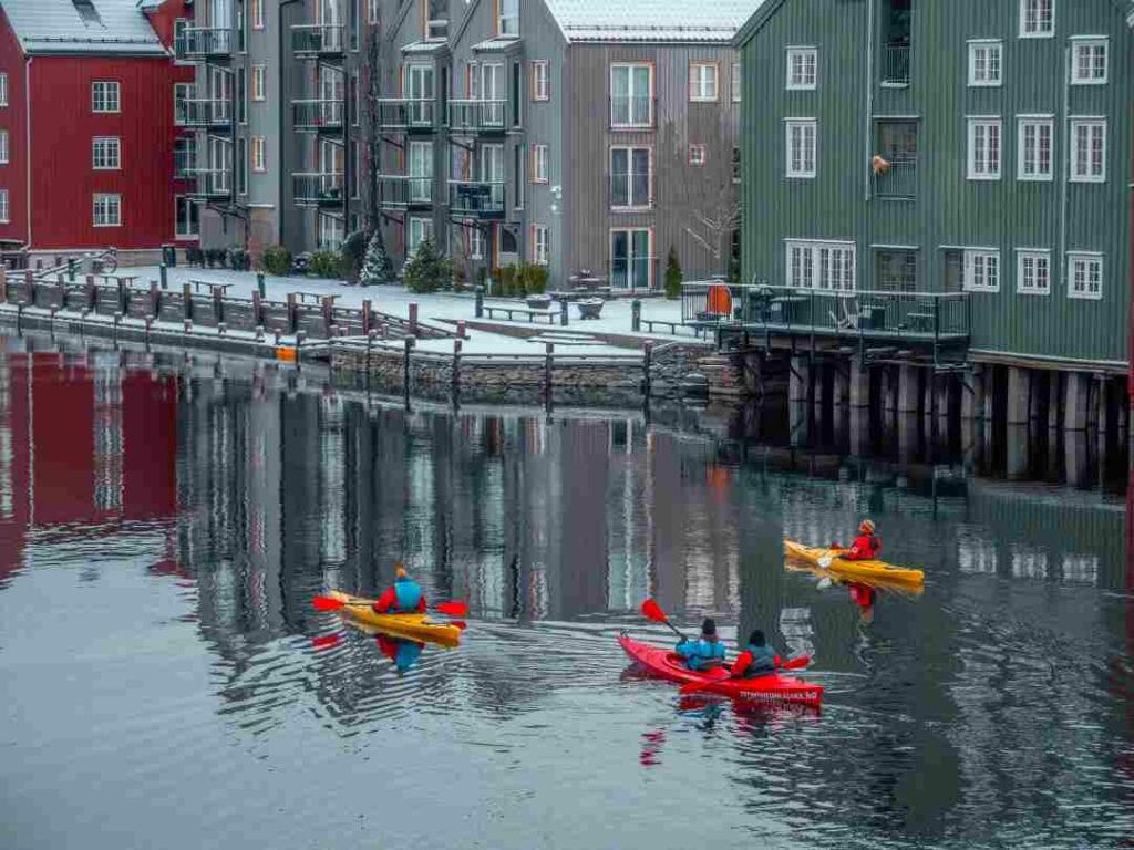 Three colorful kayaks winter paddling on a river in the middle of colorful wooden houses along the river 