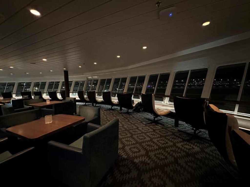 A row of comfortable chairs along a panorama window on a big ship at night where you can see the surrounding nature passing by