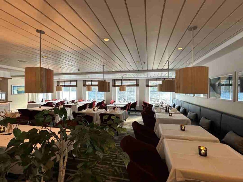 A restaurant with white table cloths and comfy seating, candle lights and Scandinavian design inside a ship where you see the water outside the windows