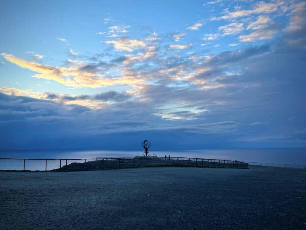 An iron globe standing on the edge of a large cliff in front of a vast ocean under blue skies in cold blue  light just after sunset