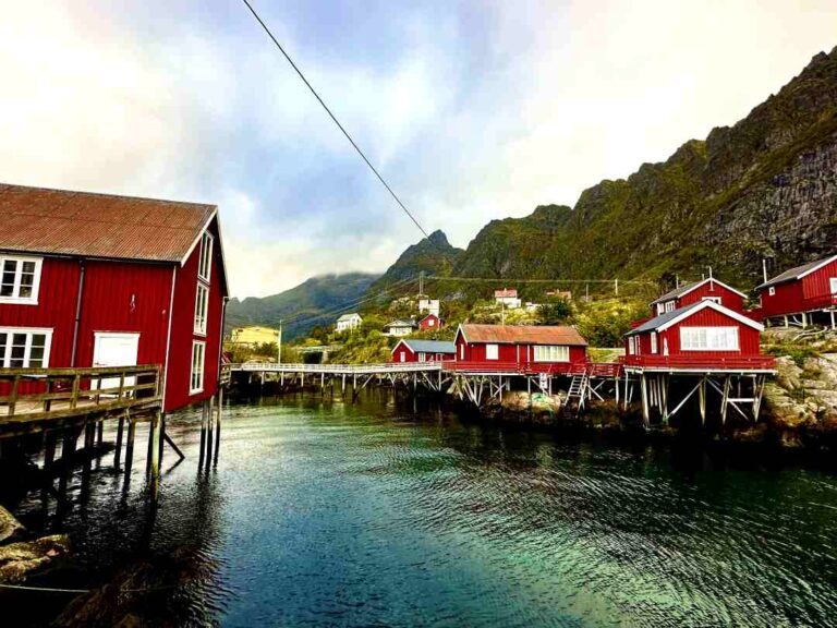 Charming red wooden fishermans cabins built over the dark green cold water in Lofoten, northern Norway on a quiet and calm Arctic day