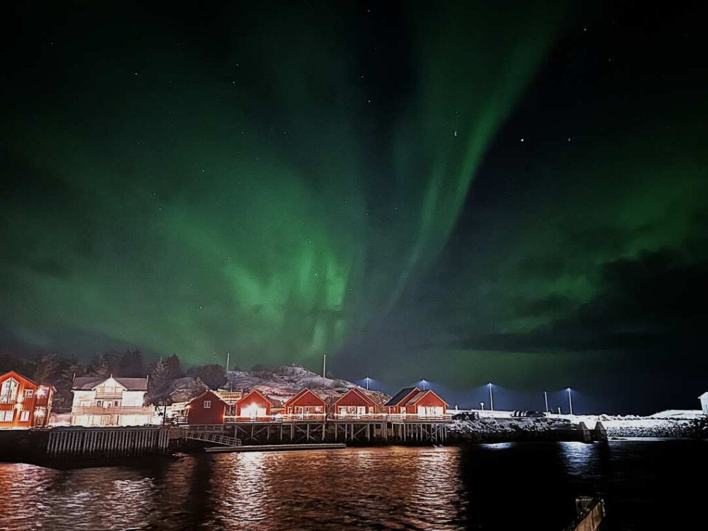 NGreen dancing northern lights in the dark sky over small, red charming fishermans cabins on an island in Lofoten, Arctic Norway