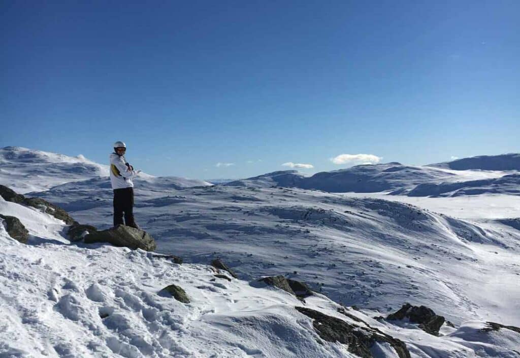 A person in skiing outfit standing on the top of a mountain in Hemsedal, Norway, on a bright sunny winter day with white mountains as far as you can see in the distance