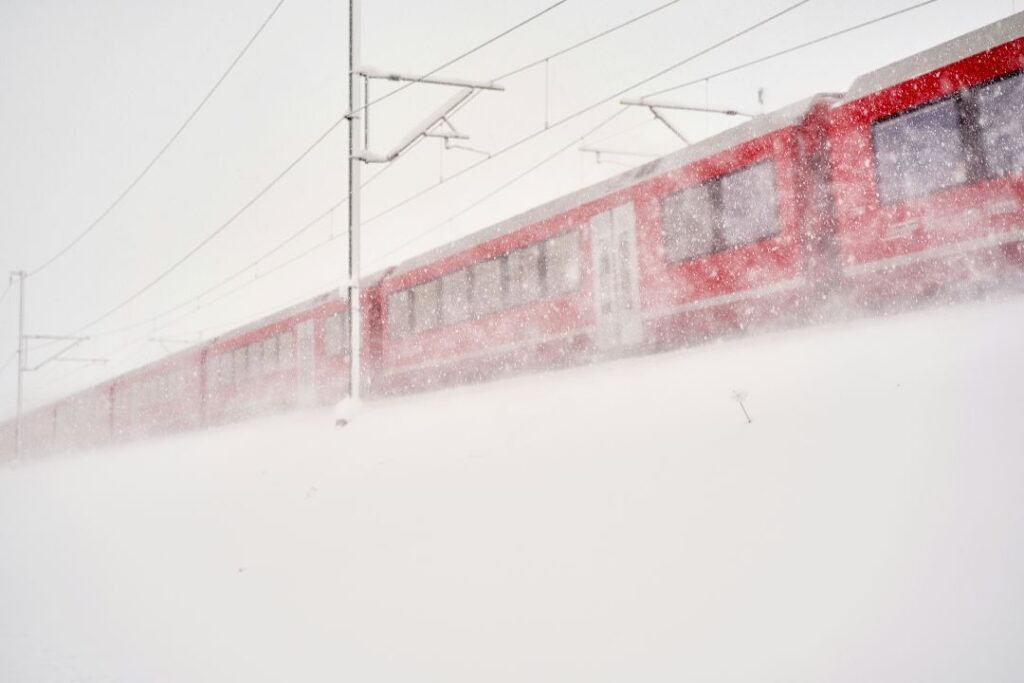 A red train in the middle of swirling white snow in the winter