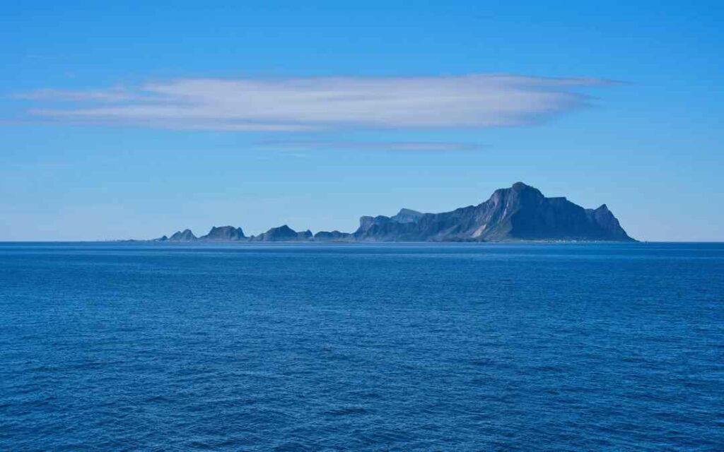 Værøy island outside Lofoten Norway in the distance on a clear sunny day, with deep blue colored sea, and a clear blue sky