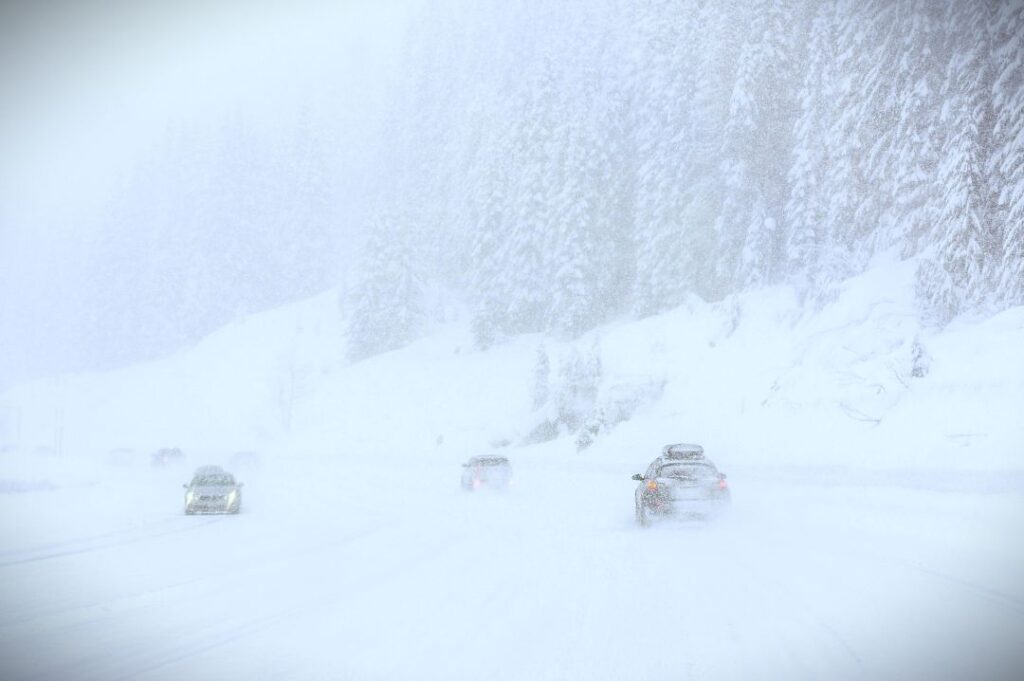 Cars on a road in the middle of a snow storm with swirling snow creating almost a white-out