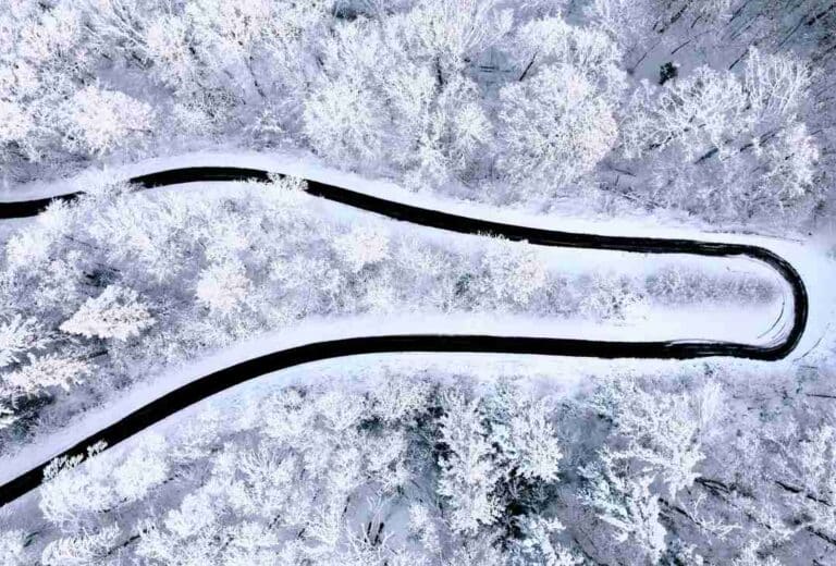 A black winding road seen from above in the middle of a white winter wonderland