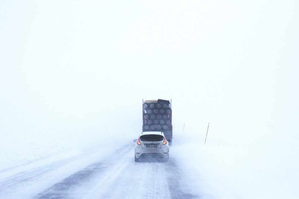 Cars on a road in a near white out during winter, the plains on either side are blindingly bright white