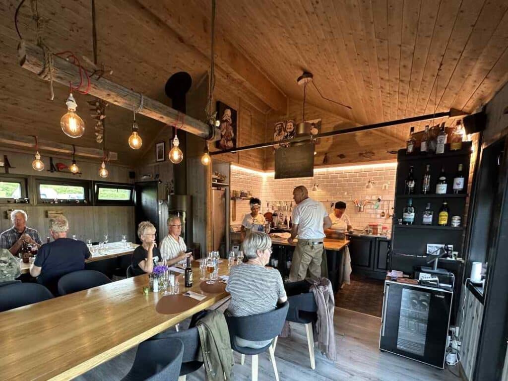 Daniels Hus - Daniels House - restaurant in Skarsvag Norway with super charming wooden Scandinavian interior mixed with dark modern details, warm lighting, and an open kitchen where you see the chefs preparing your dinner