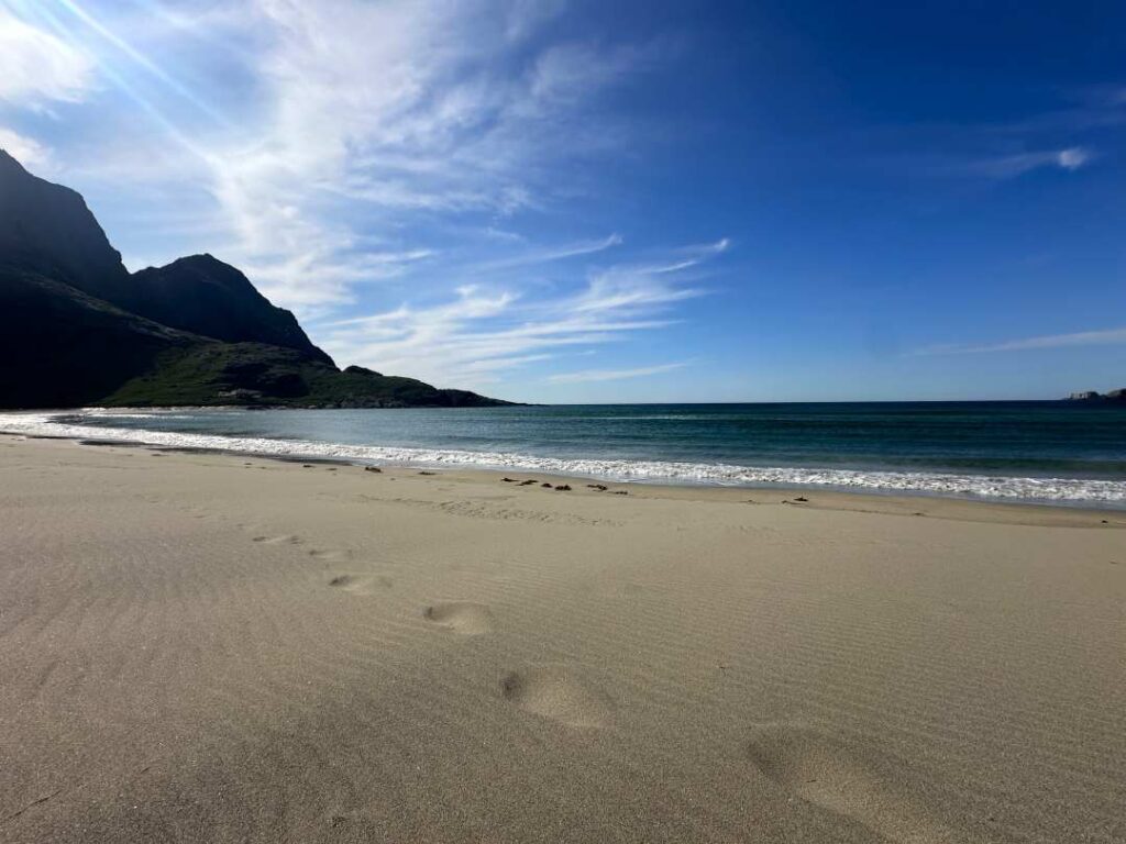 Golden sandy beach in the Arctic, in the Lofoten Islands Norway on a bright sunny day with dark green waters and whitewater waved rolling onto shore