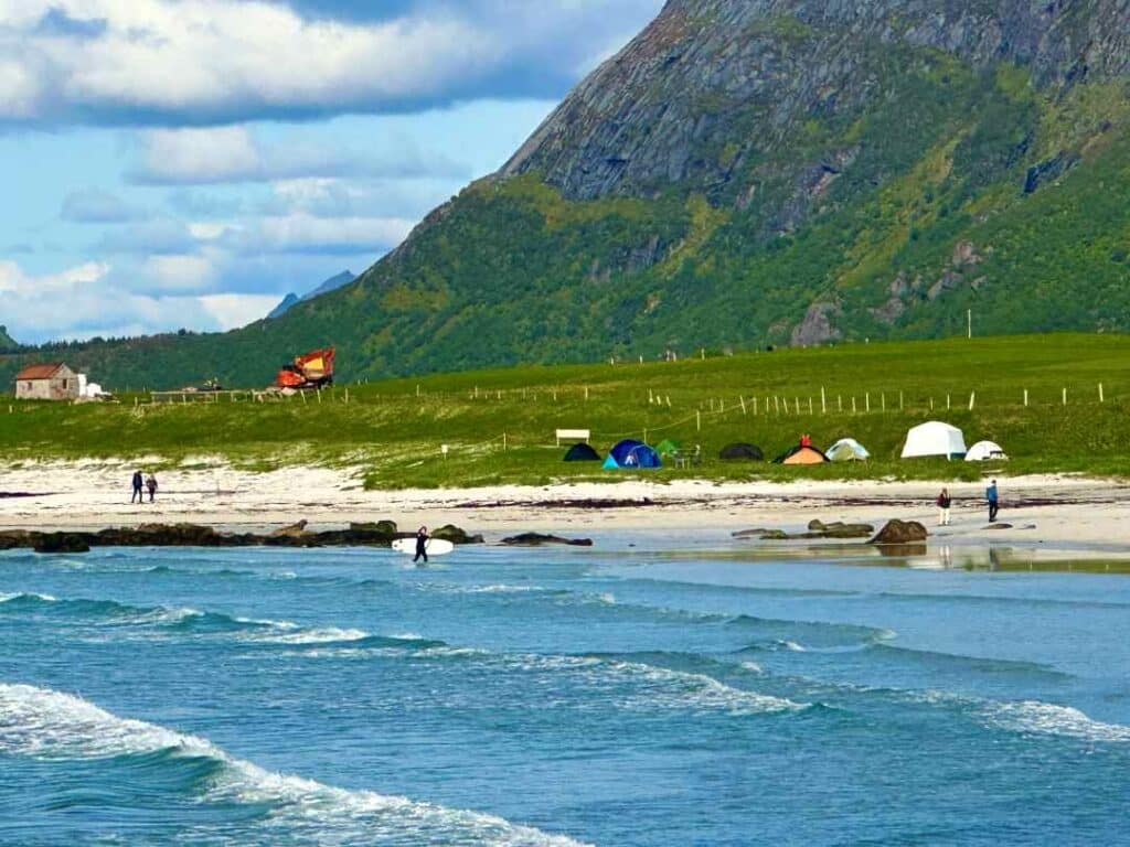 A white sandy beach under steep grey mountains colored green by the lush summer growth in Lofoten Norway