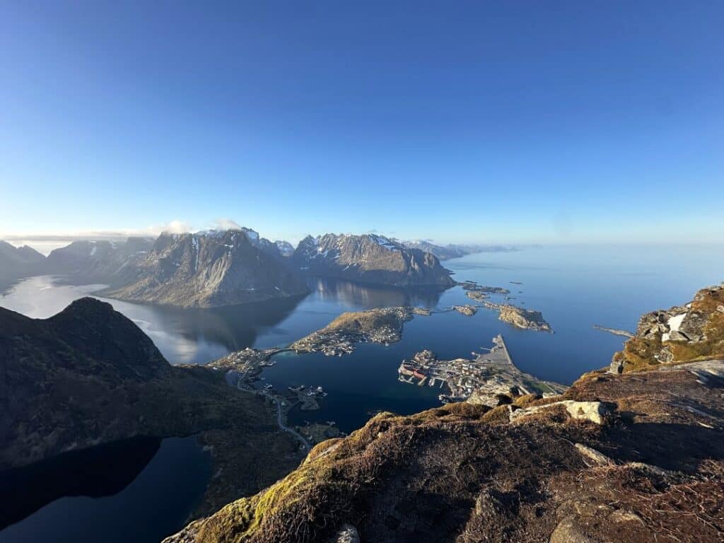 Stunning view from the top of Reinebringen mountain in Reine Lofoten on a sunny day. The deep blue sea blurs into the deep blue sky, and the majestic mountains with snowy patches stretching into the distance