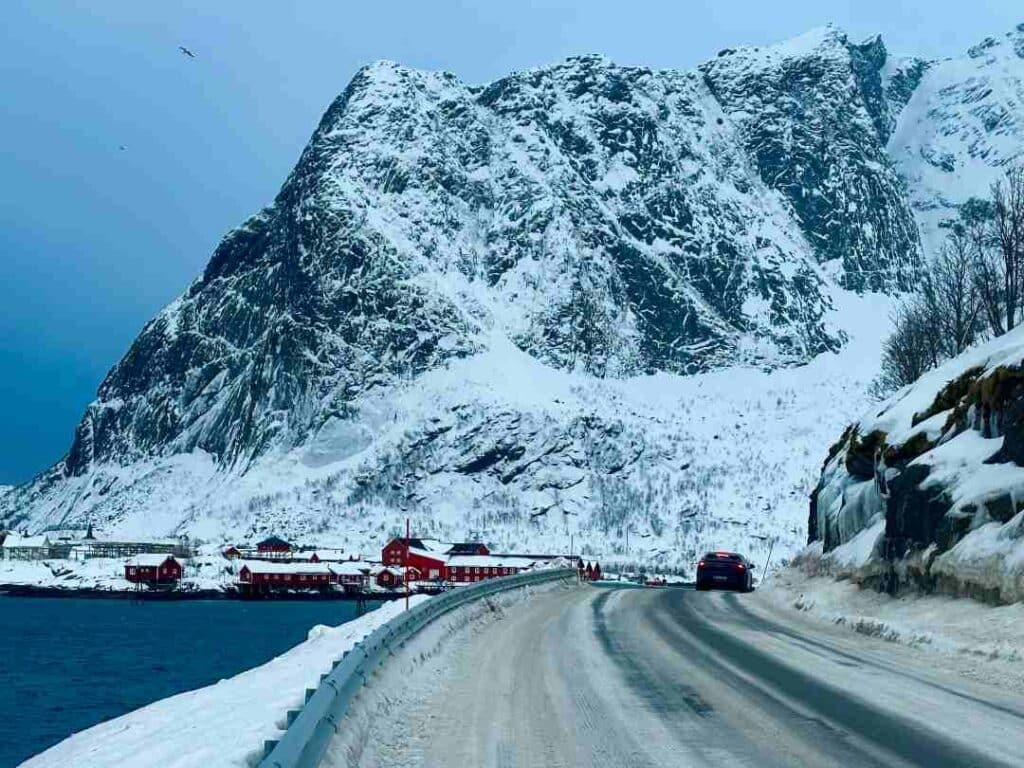 Reinebringen mountain on a clouded day in winter, seen from Andøya island and the E10 road. The mountain is covered with snow, dark patches of the rock scattered all over the mountain, under the grey sky and blue winter light of Lofoten in Arctic Norway.