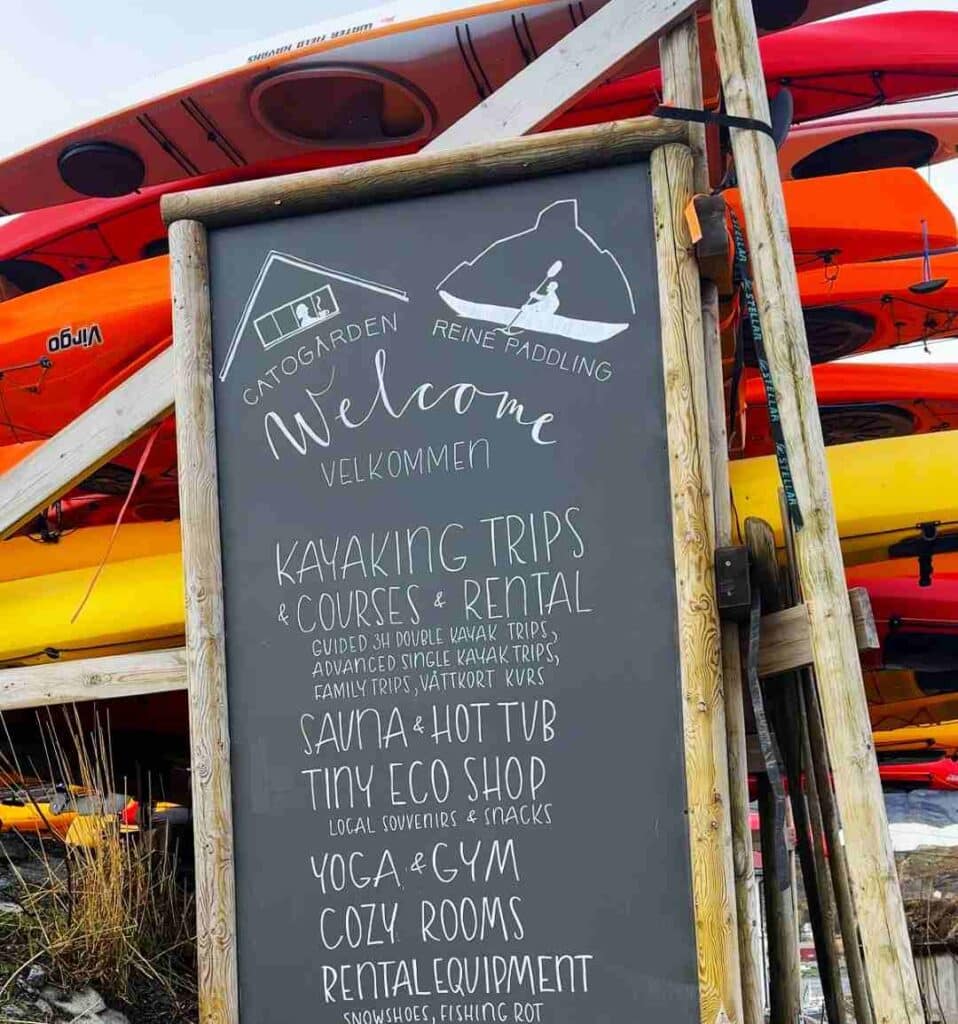 A written sign with all services at Catogården in Reine, Lofoten, who offers kayaking, sauna, hot tub, yoga, B/B and more.