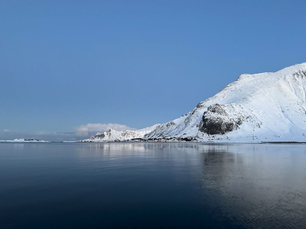 A blank blue fjord in winter, with a snow cupped mountains in thedistance, with a pale blue winter sky above