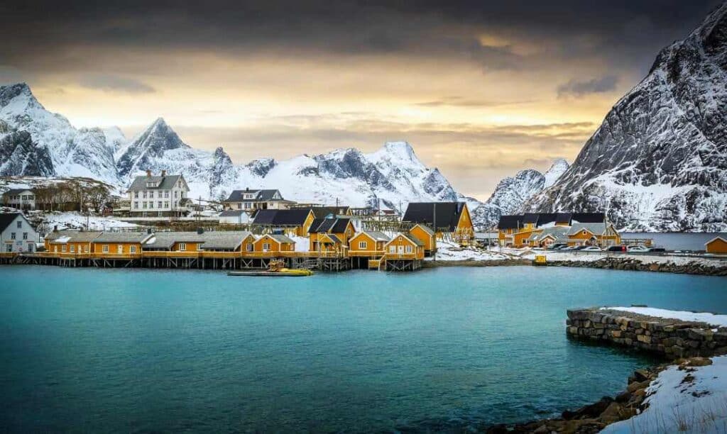Yellow fishermans cabin on an Arctic Island in Lofoten Norway in winter with the golden light of the sun behind the snow cupped mountain peaks and fjords