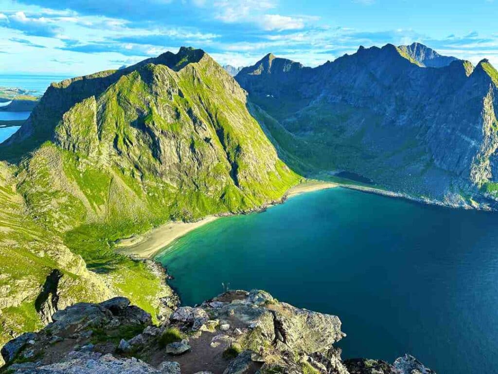 A stunning white beach seen from above from Ryten, Loftoen, surrounded by majestic mountains under a clear blue sky on a bright summer day, with crystal clear waters from the beach