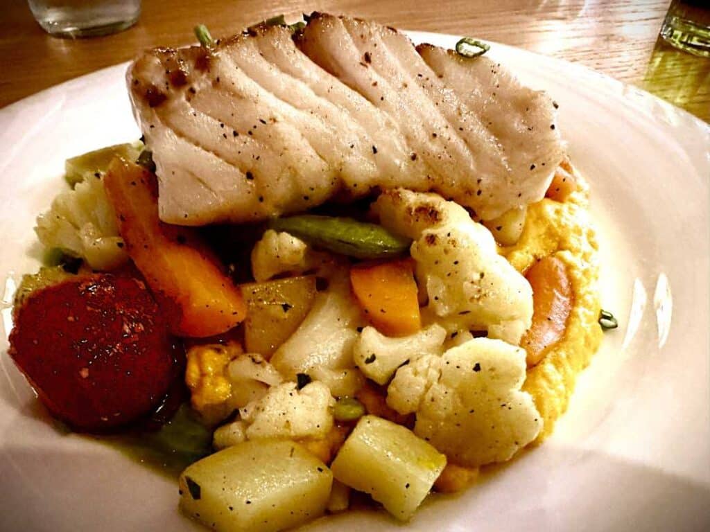 A plate of super fresh white cod fish with crispy colorful vegetables on top of a creamy potato cream