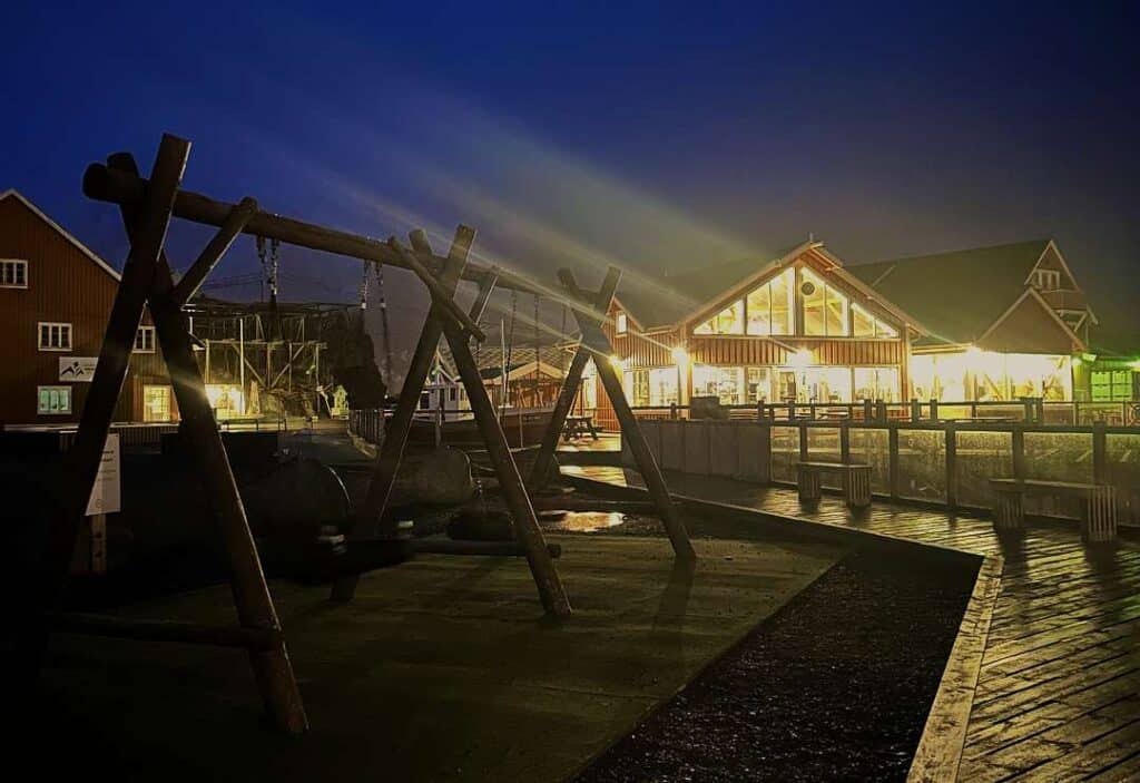 A yellow wooden building at night engulfed in golden lights, with a wooden patio walkway in front, and the dark winter sky behind it