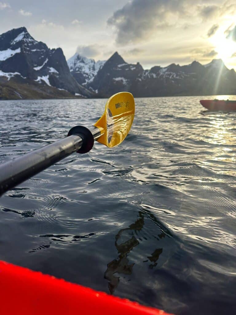 A yellow wet paddle hovering over the cold fjord waters under a hazy blue sky with mountains in the distance in Lofoten, Arctic Norway