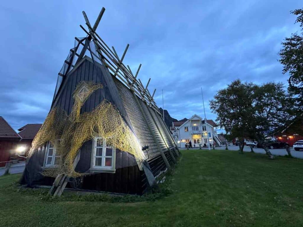 Traditional old cottages in Svolvær, Lofoten an autumn night with blue light from the sky, in front of a white wooden house with warm lights from the windows
