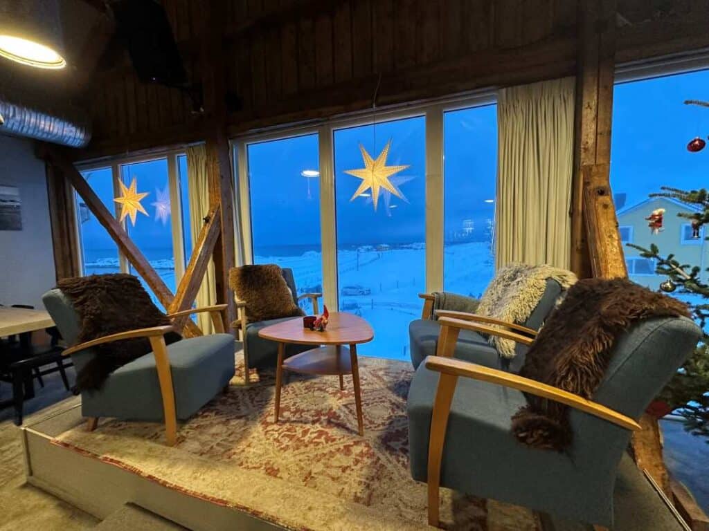A cozy table and chairs in warm light by a large window towards the winter scenery outside engulfed in blue light